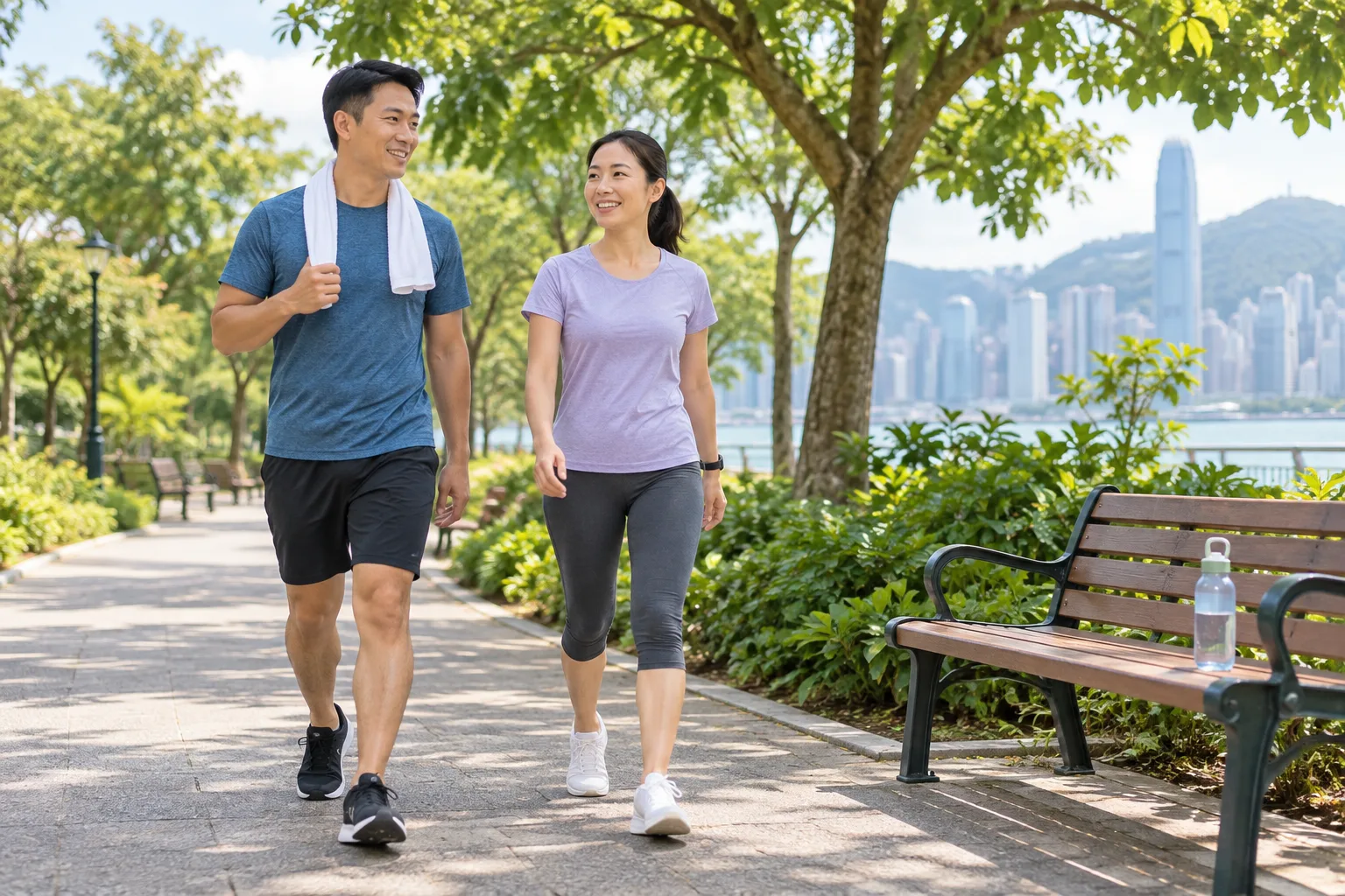 兩名成年人沿平坦公園路段放慢步伐,旁邊有長椅與水樽。